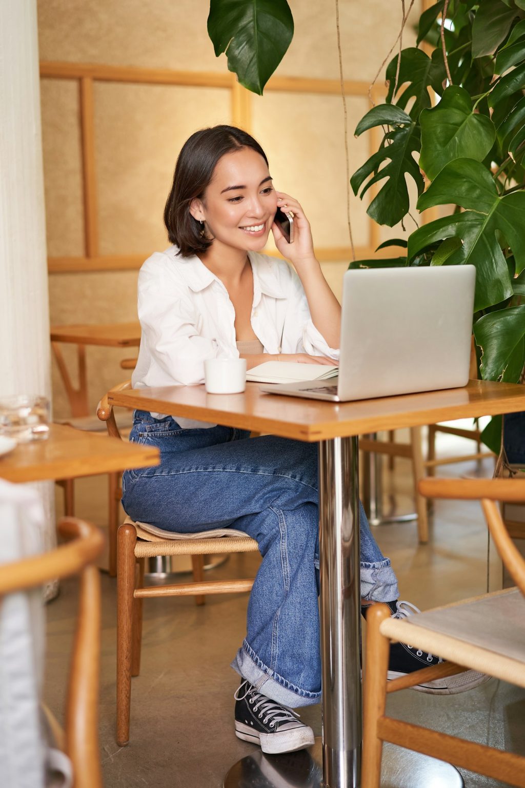 Young female cafe manager, owner sitting with laptop, answering phone calls and smiling friendly