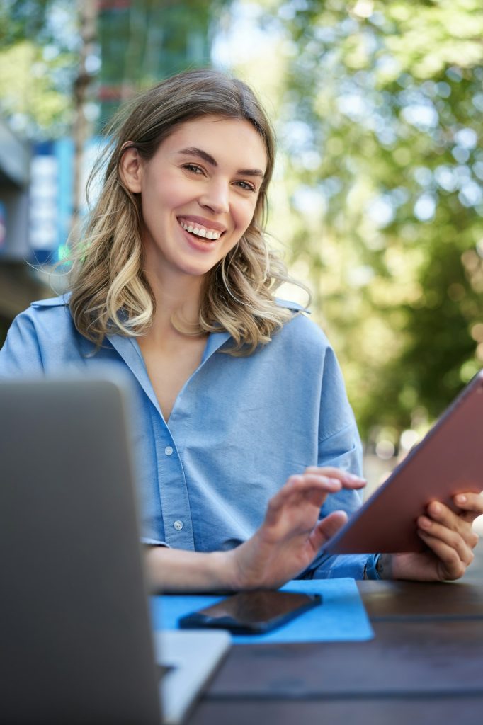 Vertical shot of smiling successful businesswoman, using digital tablet, sitting outdoors in park