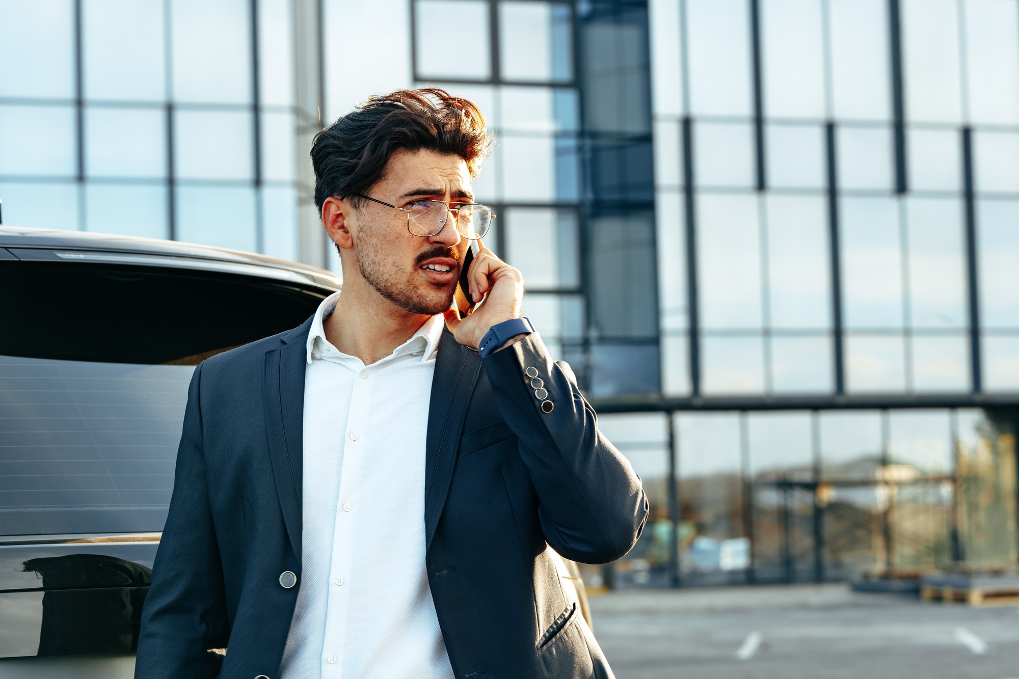 Young businessman in formal suit standing near luxury car and talking on the phone